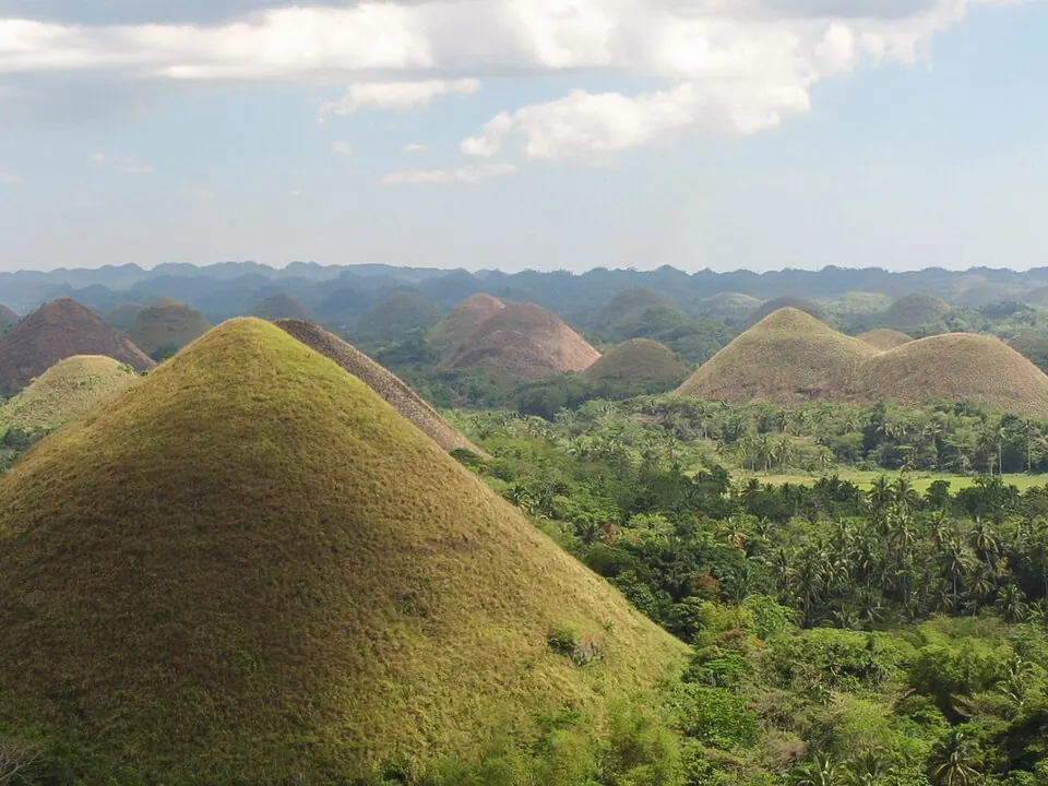 Rows of cone-shaped Chocolate Hills covered in green grass under a blue Bohol sky