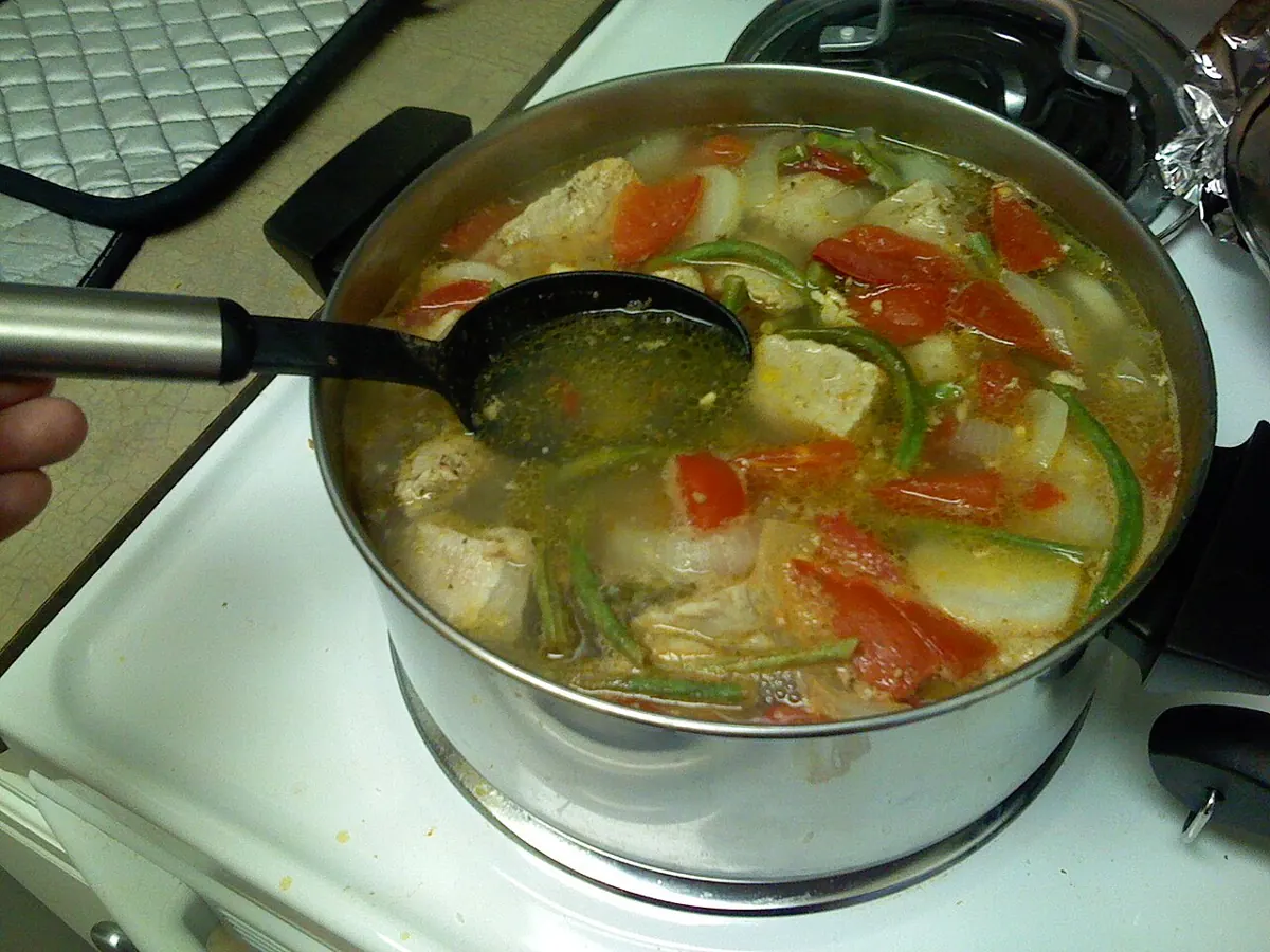 Steaming bowl of pork sinigang with kangkong, radish and tomatoes on a rainy day